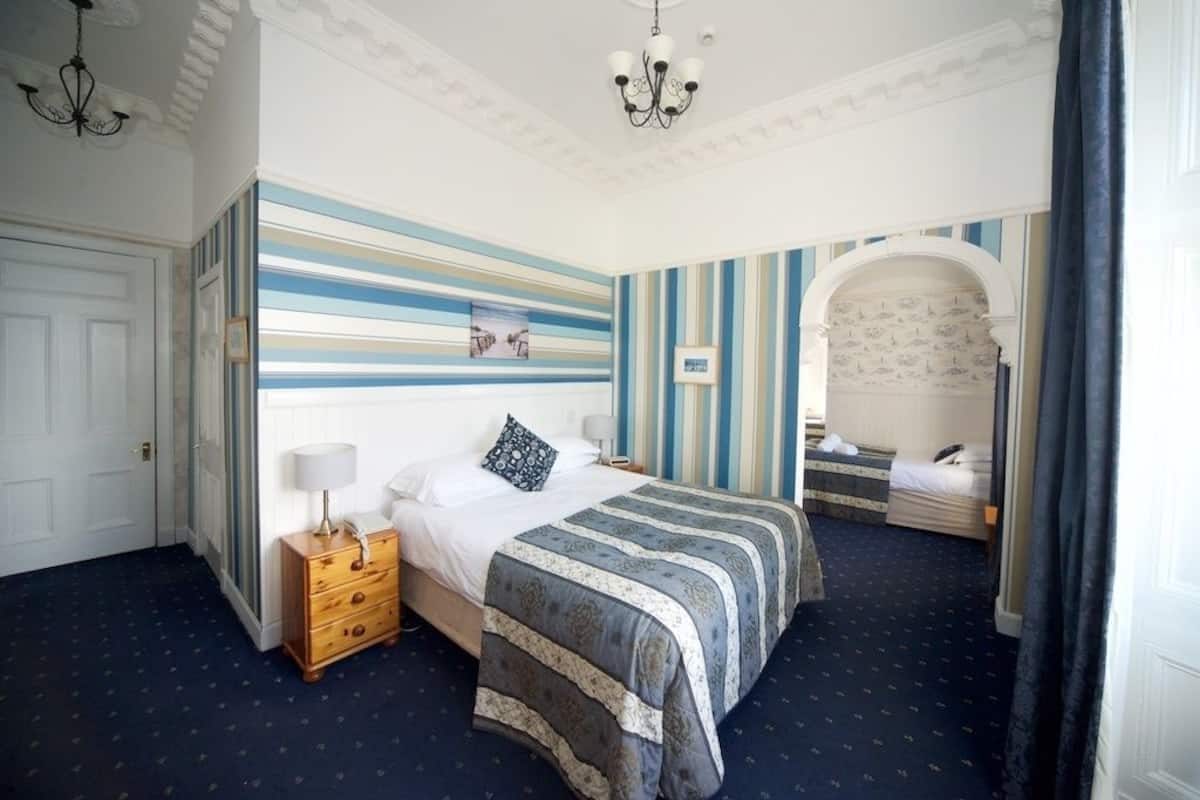 A bedroom with a large bed, a dresser, a nightstand, and a chandelier.