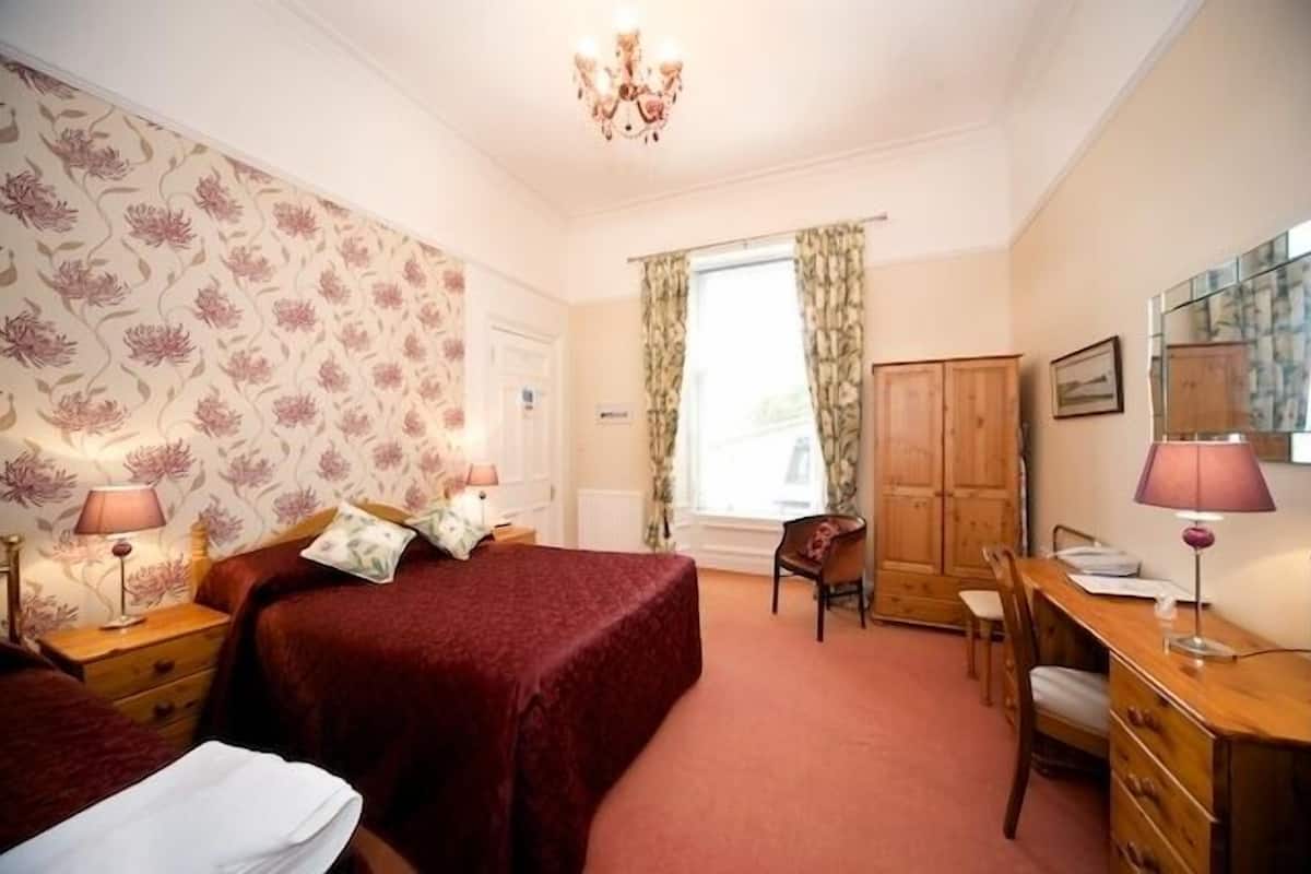 A bedroom with a bed, two bedside tables, a desk, a chair, a wardrobe, and a chandelier.