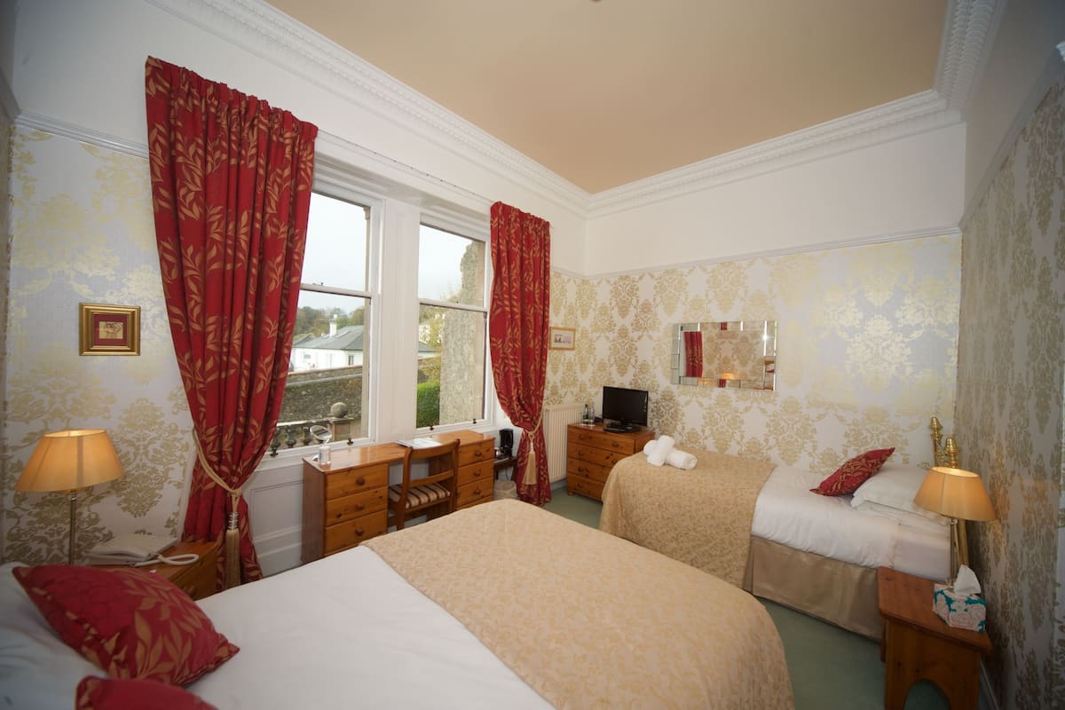 A hotel room with two beds, a desk, a chair, a television, and a window with curtains.