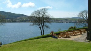 Une vue sur le lac, avec une zone herbeuse, des tables et des chaises en bois, et un banc.