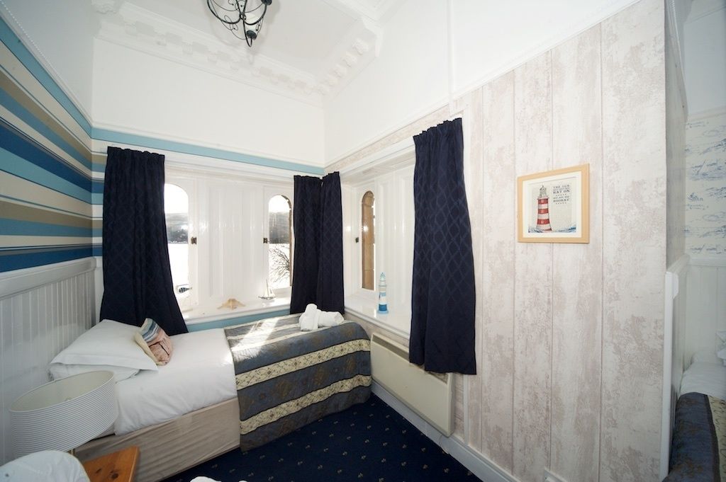 A hotel room with a bed, a window with curtains, a framed picture on the wall, and a radiator.