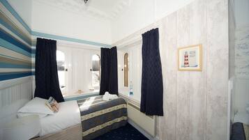 A hotel room with a bed, a window with curtains, a framed picture on the wall, and a radiator.