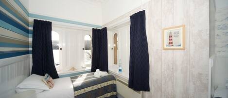 A hotel room with a bed, a window with curtains, a framed picture on the wall, and a radiator.