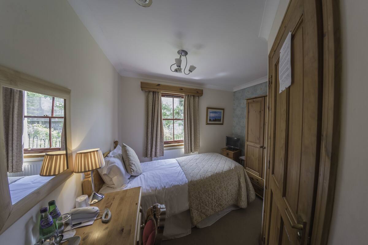 A bedroom with a bed, bedside table, lamp, and a wooden wardrobe.