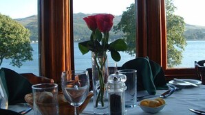 Une table dressée pour deux personnes, avec un vase de roses rouges, des verres et un salier et un poivrier.