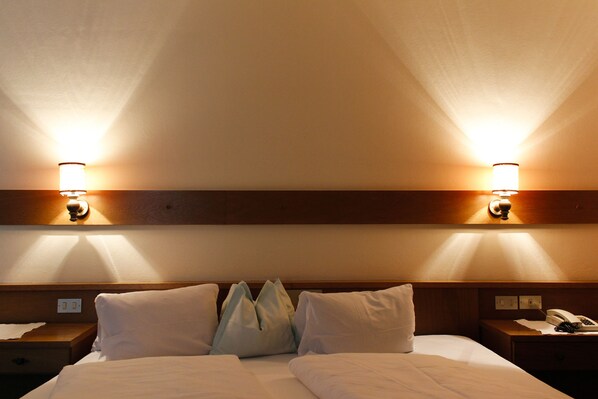 Habitación de hotel con cama, dos mesitas de noche, lámpara y teléfono fijo en la pared.