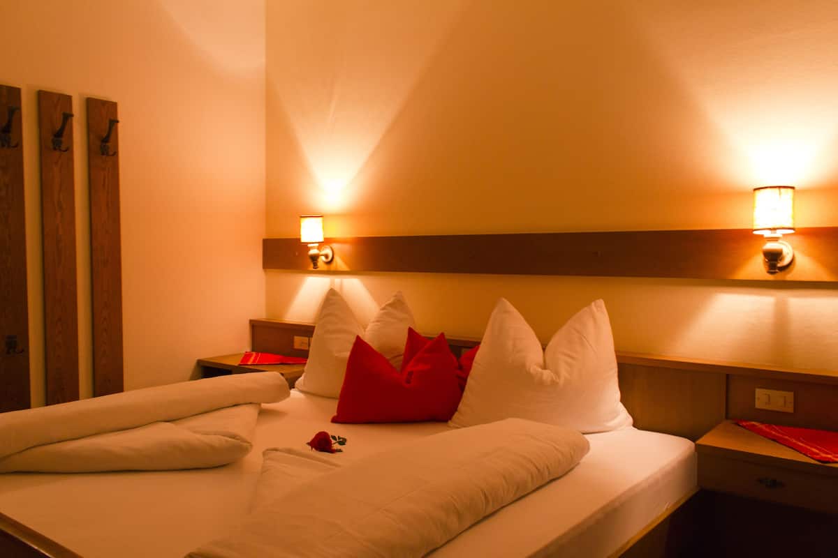 A hotel room with a neatly made bed, a nightstand, and a wall-mounted lamp.