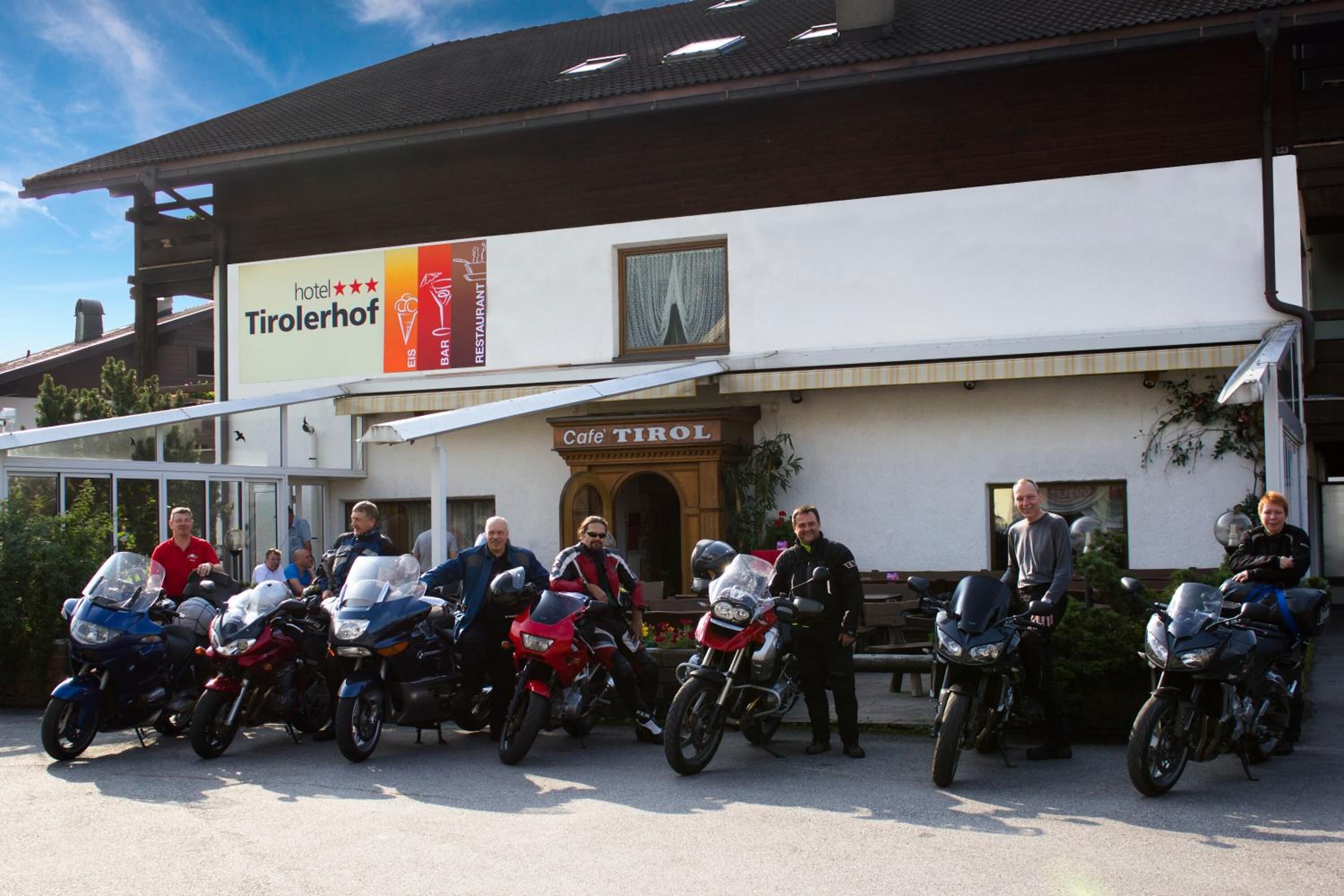 A group of people with motorcycles parked in front of a building with a sign for 'hotel Tirolhof' and 'Cafe TIROL'.