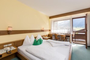A hotel room with a bed, bedside table, lamp, and a desk with chairs. - Hotel Tirolerhof (Brunico)