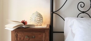 A wooden nightstand with an open book, a decorative vase, and a white pillow against a metal headboard. - Giardino Giamperduto Hotel (Bernalda)