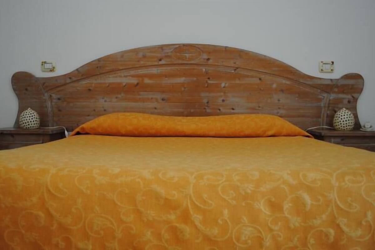A bed with a wooden headboard, an orange bedspread, and two nightstands with decorative items.
