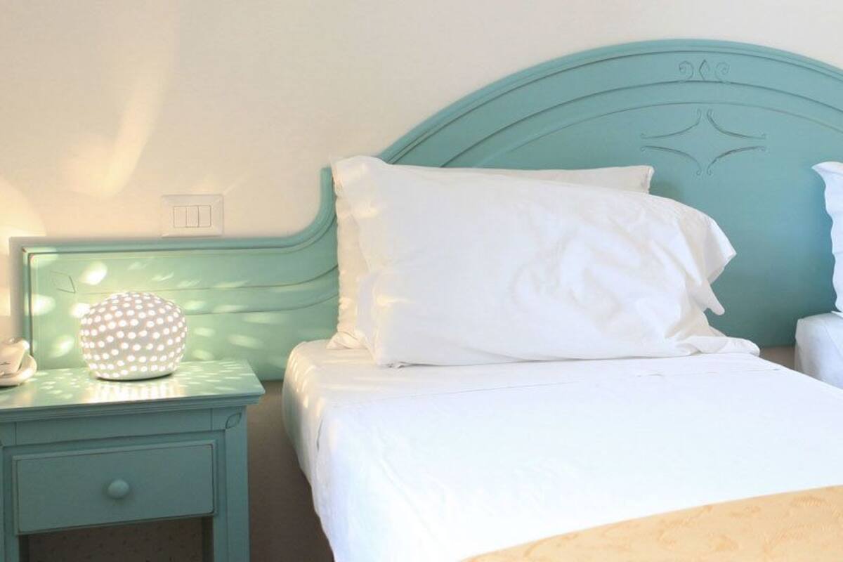 A bedroom with two beds, a nightstand with a lamp, and a wall socket.