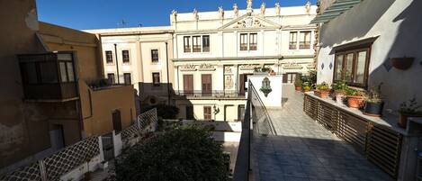 Un patio central con una escalera, rodeado de edificios con balcones y plantas en macetas.