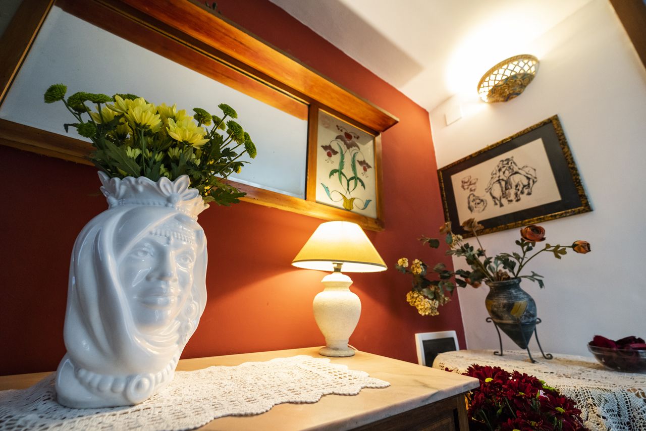 A table with a white vase of flowers, a white table lamp, and a framed picture on the wall.