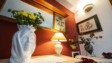A table with a white vase of flowers, a white table lamp, and a framed picture on the wall.