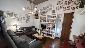 A living room with a sectional sofa, a coffee table with a vase, a bookshelf filled with books, a television, and a wooden door.