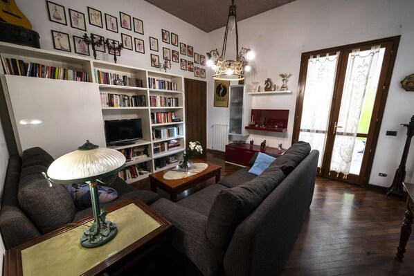 Una sala de estar con sofá, una mesa de centro, televisor, estanterías y una araña.