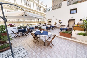 Terraza en la azotea con mesas y sillas, plantas en macetas y un paraguas blanco.