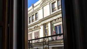 A view through a window with a metal railing, looking out onto a street with buildings and flags.