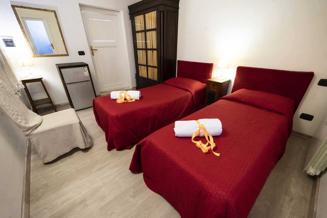 Habitación de hotel con dos camas individuales, un escritorio pequeño, un refrigerador y un armario.