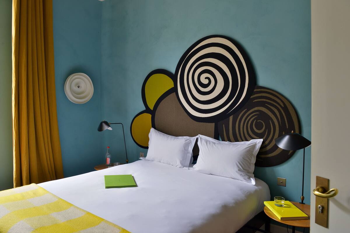 Una habitación de hotel con una cama, una mesita de noche, una lámpara y una pared con arte abstracto.