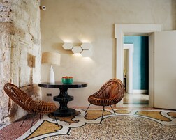Una habitación con una mesa redonda, dos sillas de mimbre, un frutero, una lámpara y una luz de pared hexagonal.