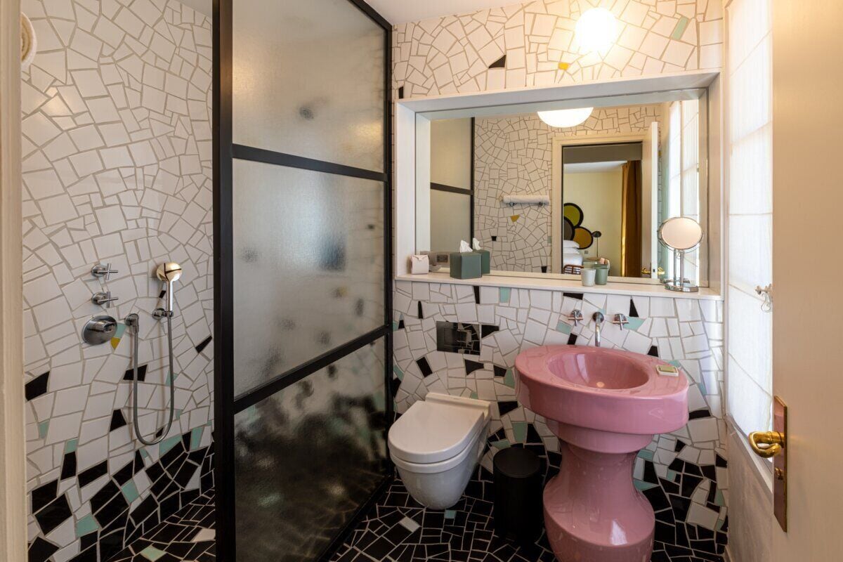 A bathroom with a mosaic tile wall, a toilet, a sink, and a shower.