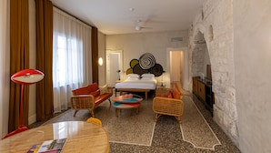 A hotel room with a bed, two sofas, a coffee table, a TV, and a stone wall. - Hôtel du Cloître (Arles)