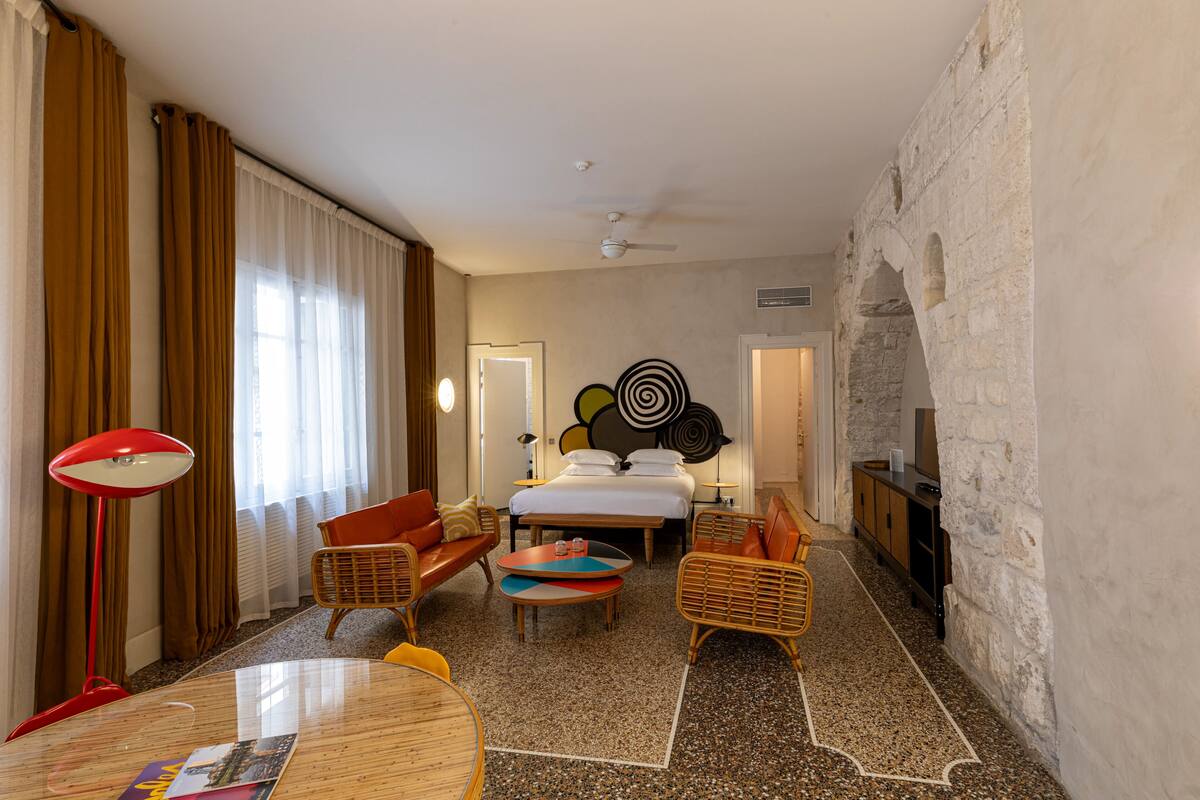 Habitación de hotel con cama, dos sofás, una mesa de centro, televisión y pared de piedra.