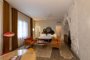 A hotel room with a bed, two sofas, a coffee table, a TV, and a stone wall. - Hôtel du Cloître (Arles)