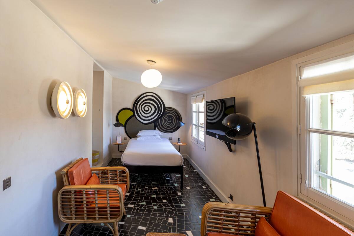 Una habitación de hotel con una cama, dos sillas, un televisor y una ventana.