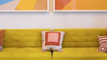 A bright yellow sofa with two pillows, a geometric abstract painting, and another abstract painting on the wall.
