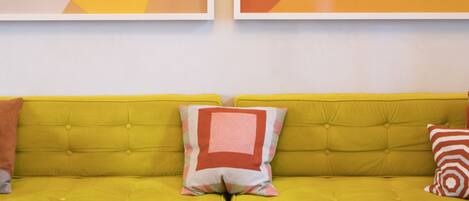 Un canapé jaune vif agrémenté de deux coussins, une peinture abstraite aux motifs géométriques et une autre peinture abstraite accrochée au mur.