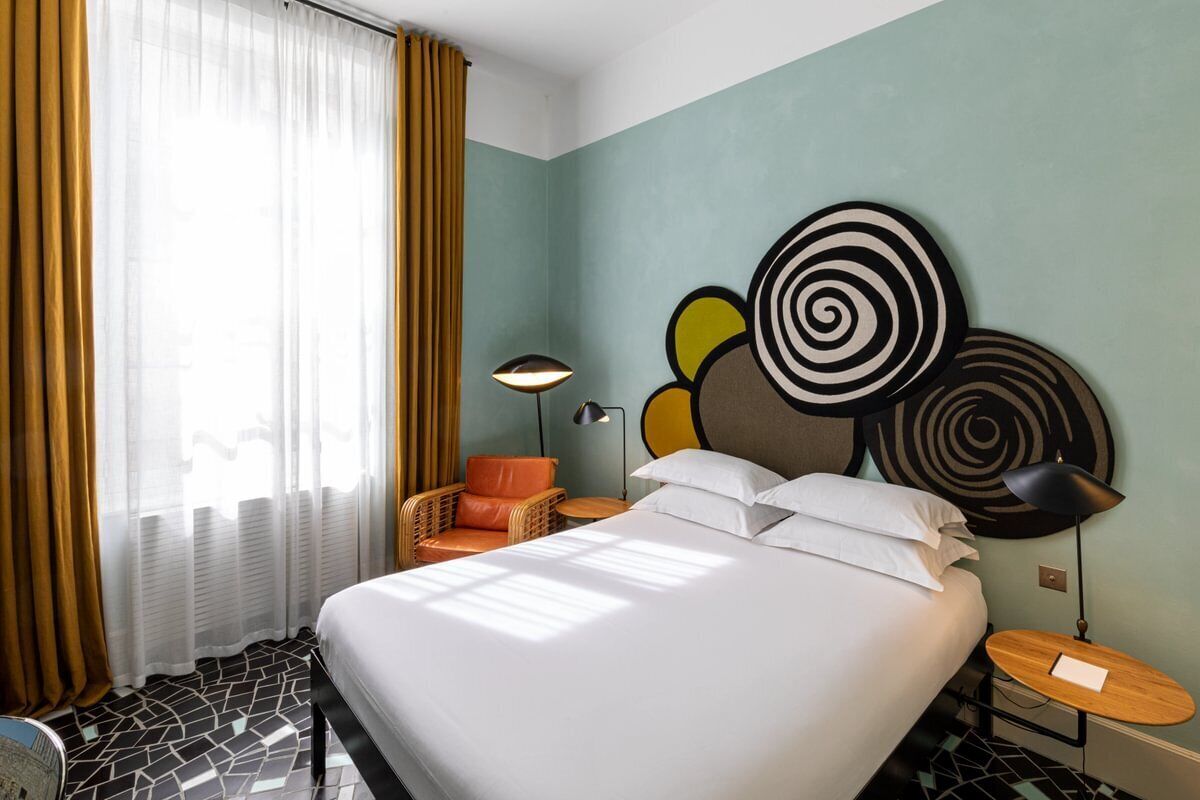 Habitació d'hotel amb un llit, una cadira, una làmpada i una decoració mural.