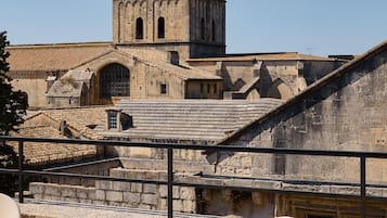 Une tour historique dotée de fenêtres en arc de cercle et d’un balcon donnant sur une terrasse aménagée avec des sièges extérieurs.