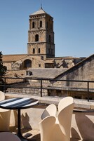 Una torre histórica con ventanas en arco y un balcón que da a una terraza con mobiliario exterior.