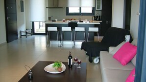 A modern living room with a sofa, a coffee table, and a kitchen in the background. - Sugar and Almond - Luxury Apartments (Corfu)