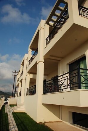 A modern multi-story building with balconies and a paved walkway. - Sugar and Almond - Luxury Apartments (Corfu)