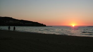A beach at sunset with two people walking along the shore. - Sugar and Almond - Luxury Apartments (Corfu)