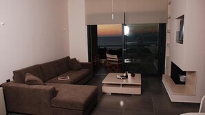 A modern living room with a sofa, coffee table, and a view of the ocean through a glass door. - Sugar and Almond - Luxury Apartments (Corfu)