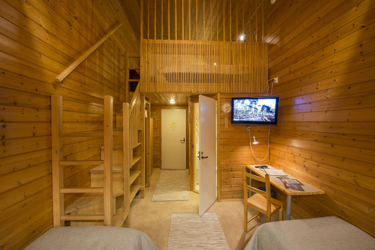A wooden cabin interior with a TV, a desk, and two beds.