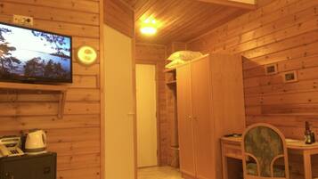 A wooden interior with a television on the wall, a wardrobe, a desk with a chair, and a bed.