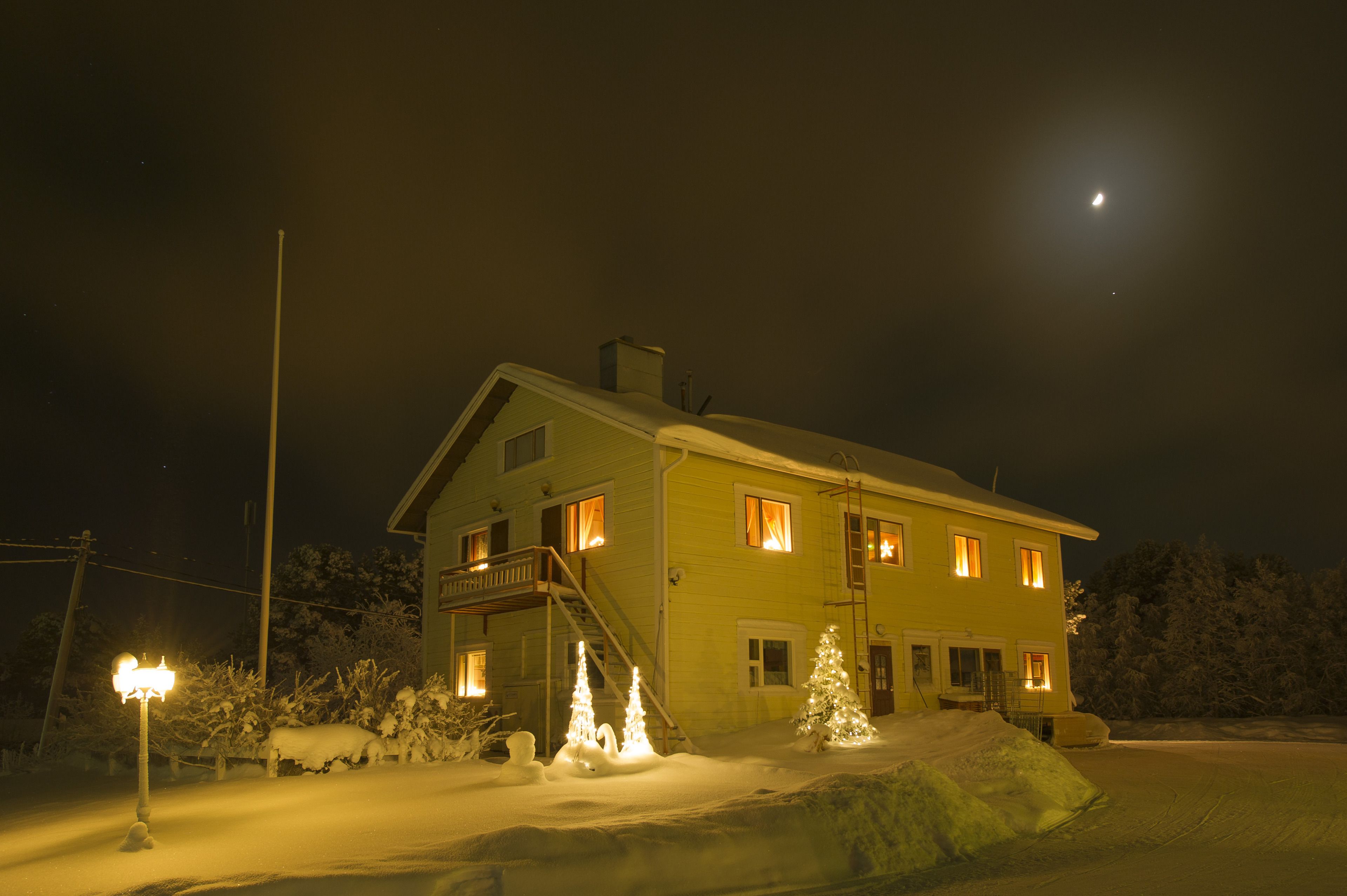 Ett tvåvåningshus med en balkong, en trappa som leder upp till andra våningen och ett snötäckt landskap.