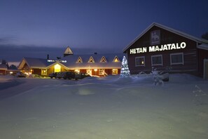 Ein schneebedecktes Gebäude mit der Aufschrift "Hetan Majatalo" und einem Weihnachtsbaum davor.