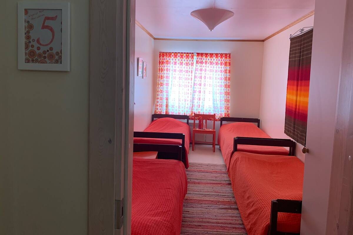 A room with three single beds, a wooden chair, a table, and a ceiling light.