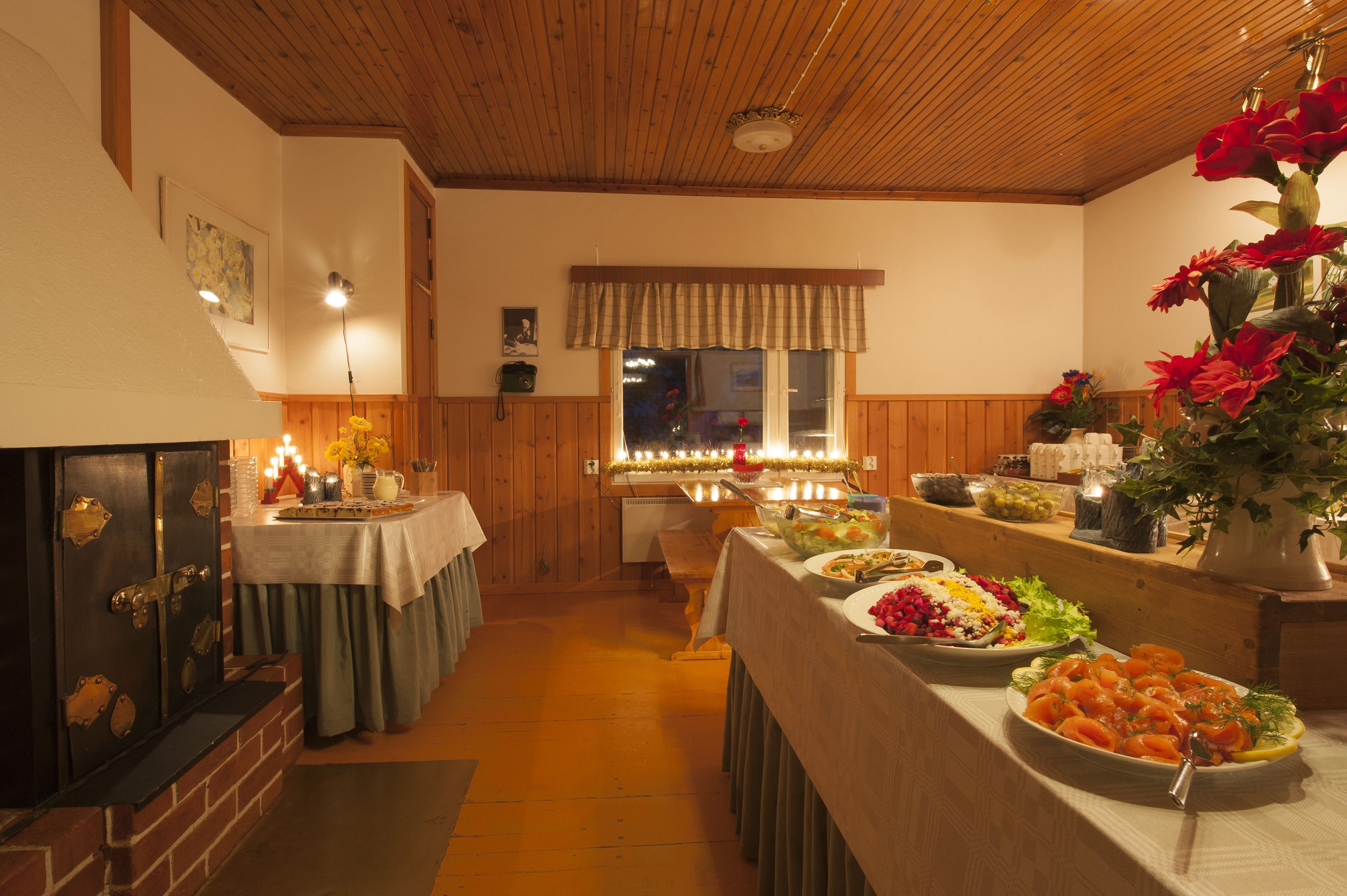 A cozy dining area with wooden walls and a fireplace, featuring a buffet table with various dishes and a vase of flowers.