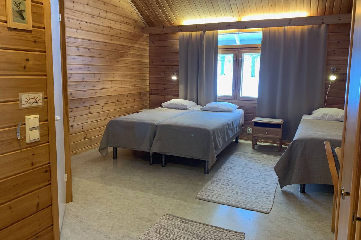 A wooden cabin bedroom with two beds, a nightstand, and a window with curtains.