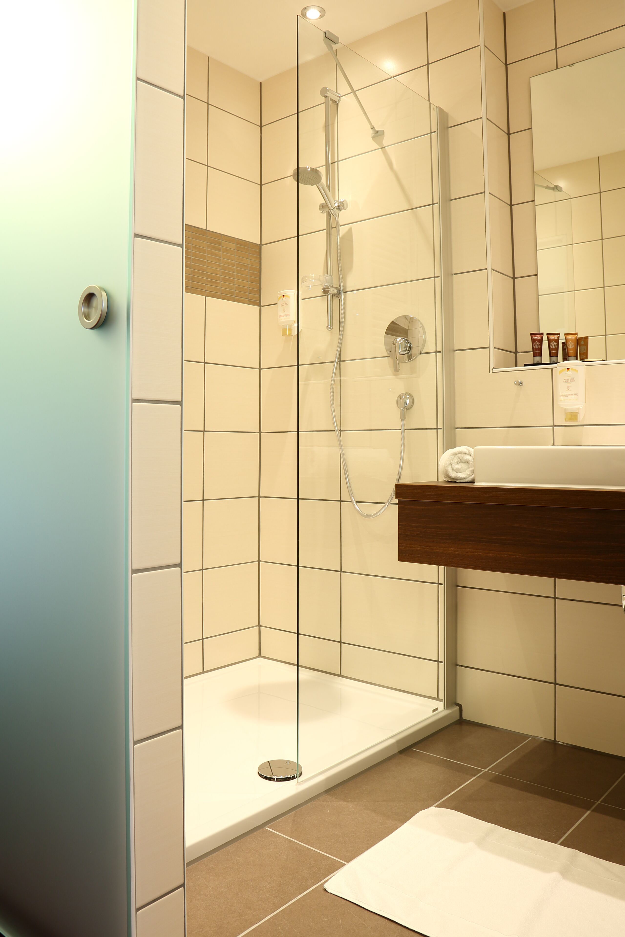 Un baño moderno con ducha envuelta en cristal, tocador de madera y espejo sobre el lavabo.
