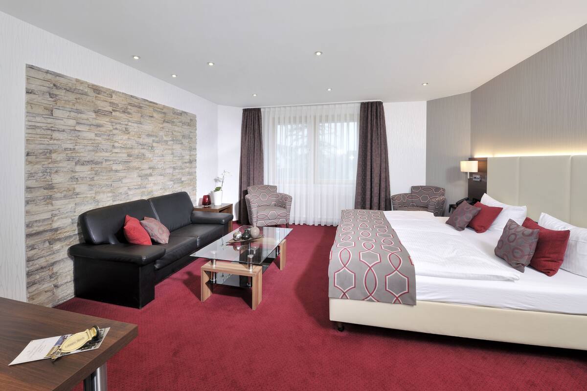 A hotel room with a large bed, a sofa, a coffee table, and a stone accent wall.