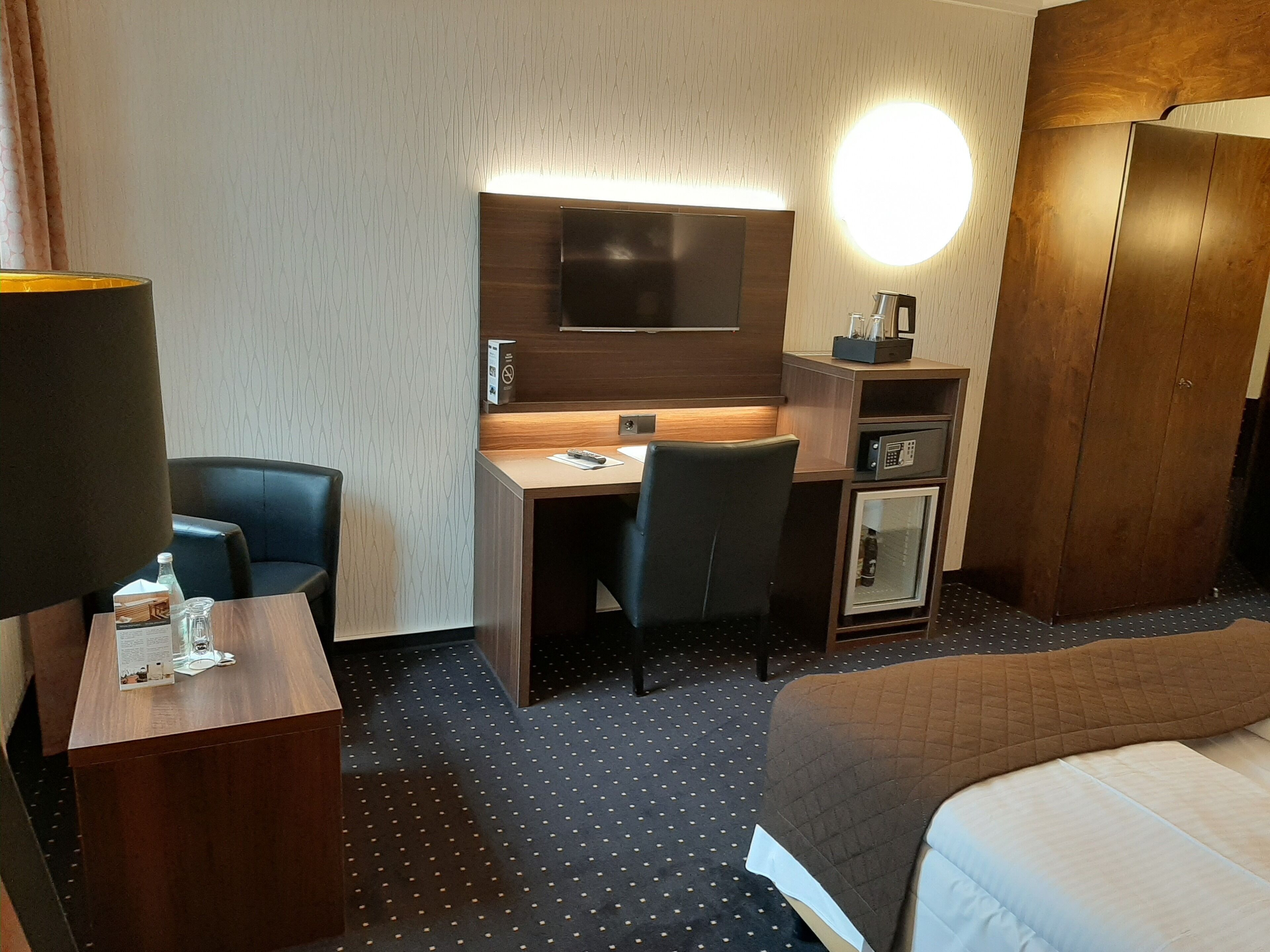 Une chambre d’hôtel comprenant un lit, un bureau avec une chaise, une télévision, un minibar et une armoire.